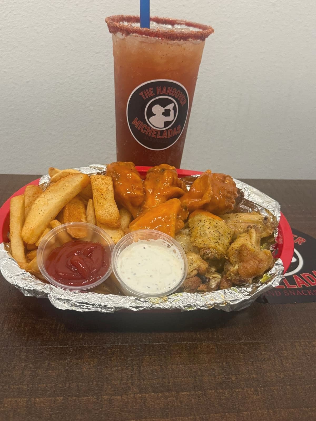 Rimmed michelada next to a basket of wings and wedge fries